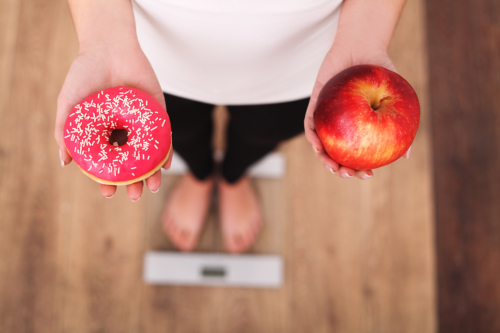 Eine Frau steht mit Donut und Apfel auf der Waage